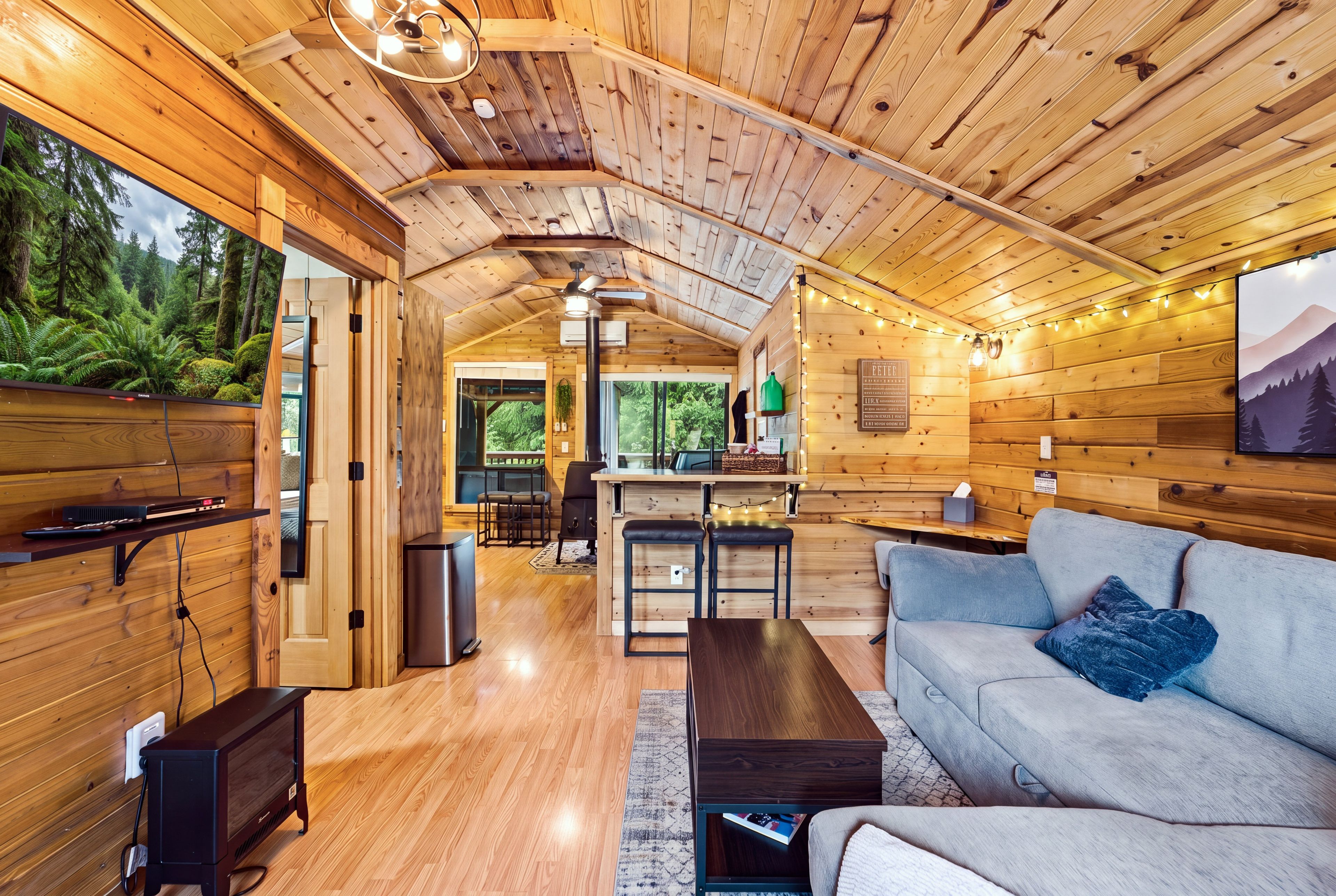 A cozy cabin interior with a wooden ceiling, a sofa, a coffee table, and a kitchen area.
