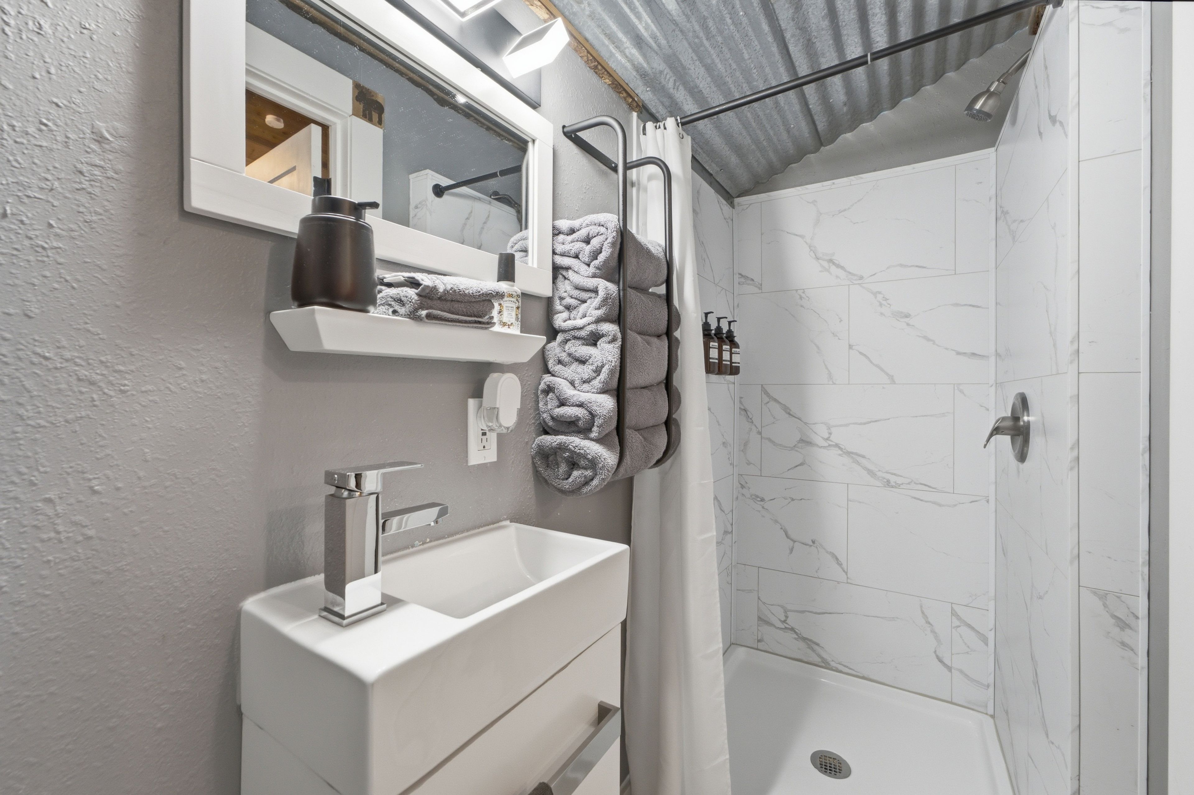 A bathroom with a white sink, a mirror, a towel rack with towels, and a shower area with a white shower curtain.