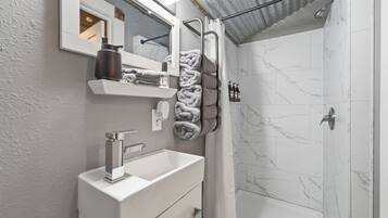 A bathroom with a white sink, a mirror, a towel rack with towels, and a shower area with a white shower curtain.