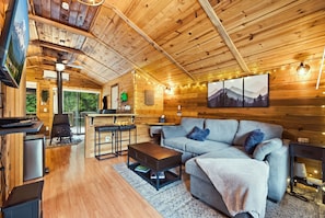 A cozy cabin interior with a wooden ceiling, a sofa, a coffee table, a TV, and a fireplace. - Perch - Whispering Pines | Romantic Rainier Cabin + Hot Tub (Ashford)