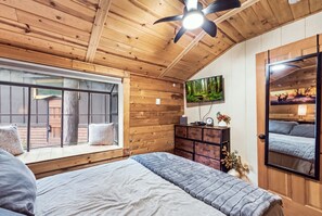 Quarto aconchegante com cama, escrivaninha, televisão e janela com vista para um terraço.