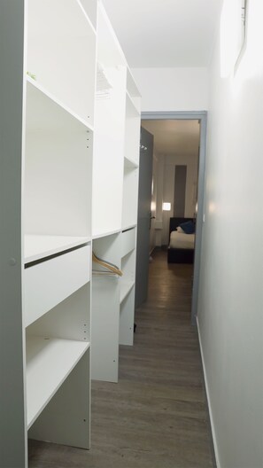 Ein schmaler Flur mit weißen Regaleinheiten an einer Seite und einem Bett mit blauer Decke am Ende des Raumes.