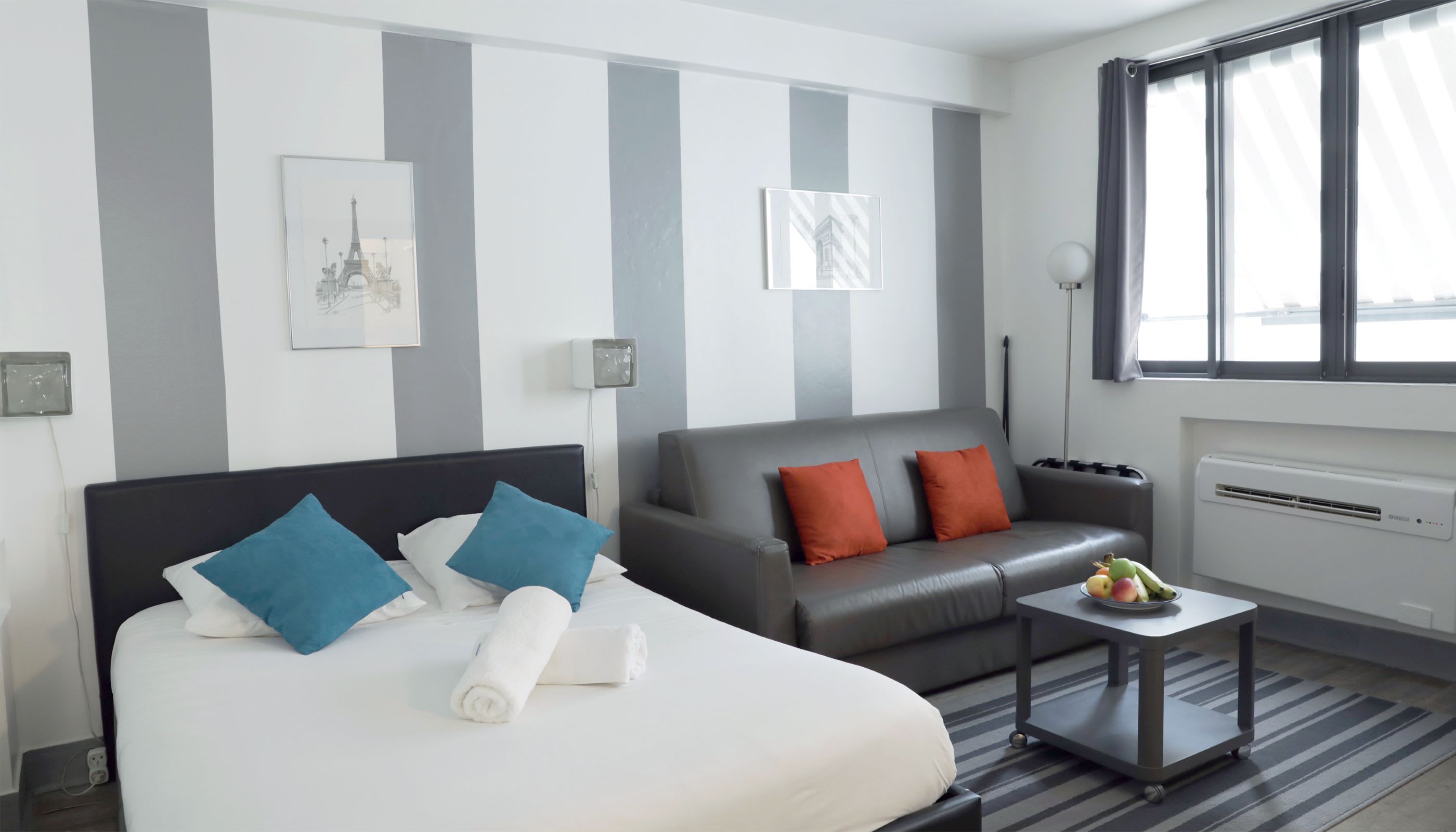 A hotel room with a bed, a sofa, a small table with fruits, and a radiator.