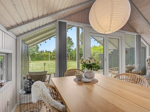 Een ruime kamer met een grote houten tafel, rieten stoelen en uitzicht op een groen landschap door grote ramen.