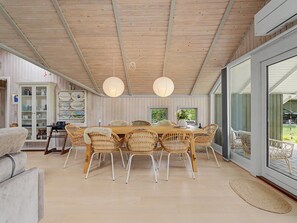 Een eethoek met een houten tafel, rieten stoelen en een glazen deur naar buiten.