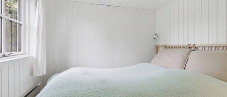Un dormitorio con cama, ventana y lámpara de pared.