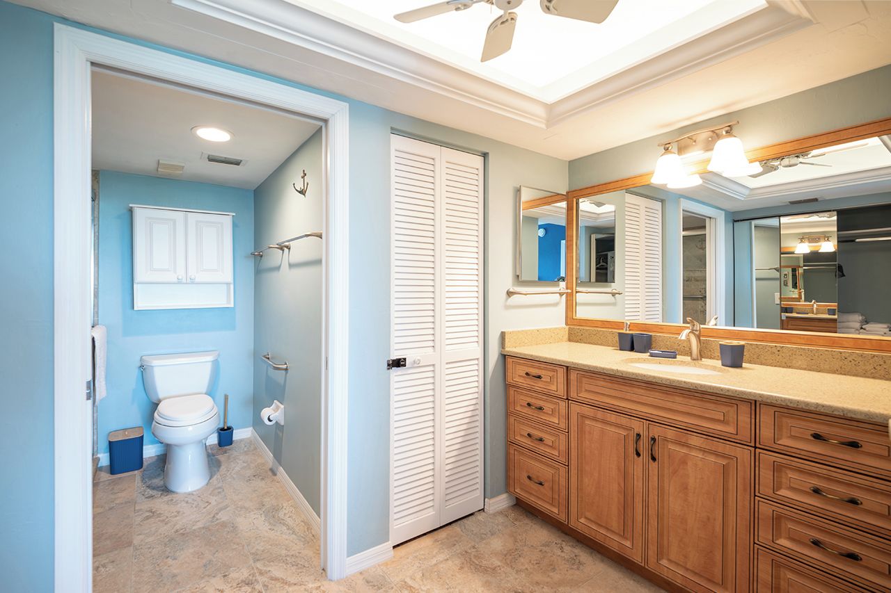 A bathroom with a toilet, a mirror, wooden cabinets, and a ceiling fan.
