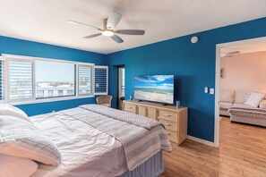 Un dormitorio con cama, televisor, cómoda y ventana con persianas.