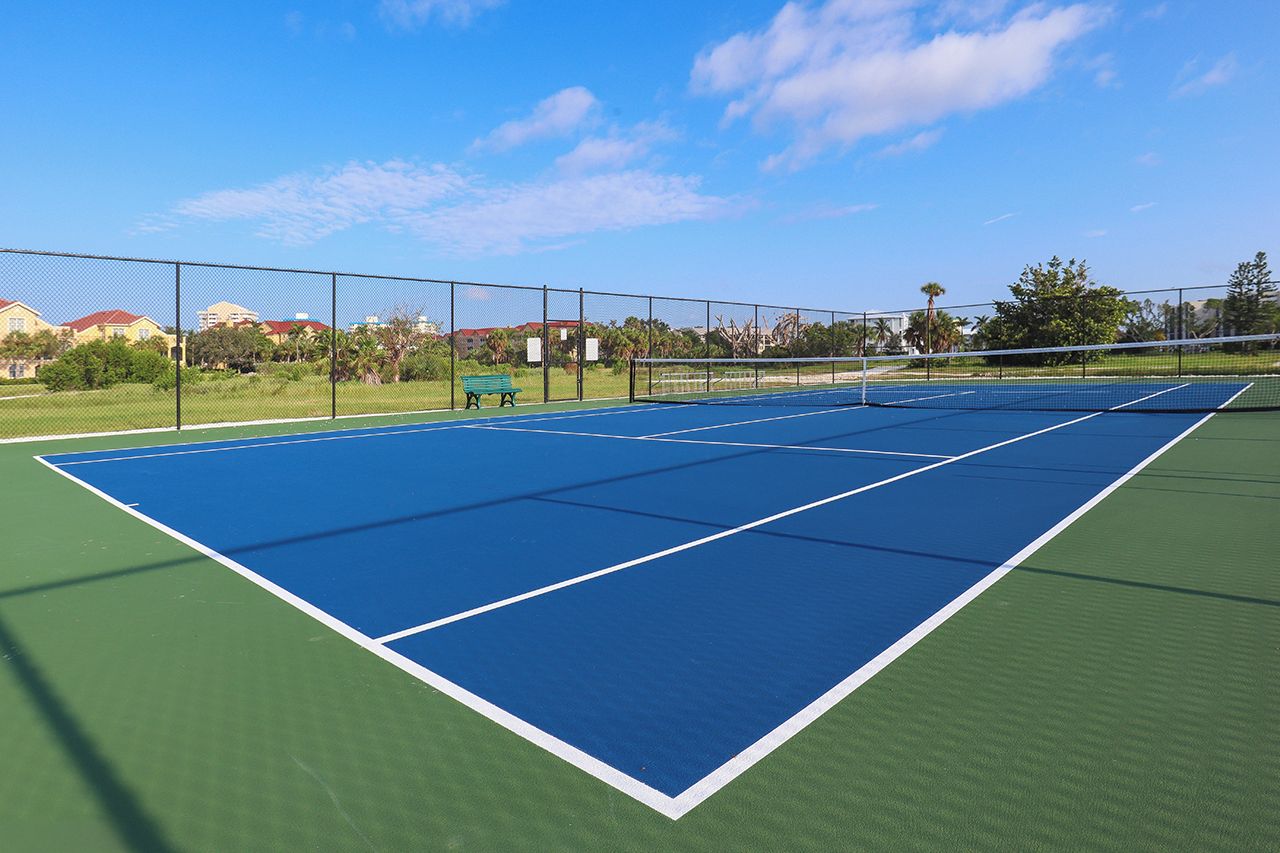 A tennis court with a net, surrounded by a fence, and a bench in the background.