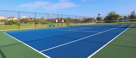 A tennis court with a net, surrounded by a fence, and a bench in the background.