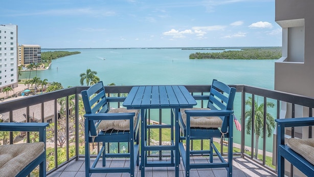A balcony with a table and chairs, overlooking a body of water and distant land. - 2B/2B HARBOUR POINTE CONDO 715 ON THE BAY, FISHING DOCK, WALK TO BEACH! (Fort Myers Beach)