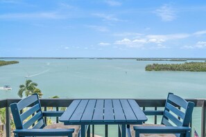 Vista desde un balcón con mesa y sillas, con vista a aguas tranquilas, tierra distante y cielo despejado.