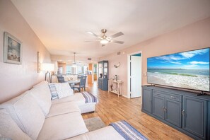 A living room with a sofa, TV, and a view of the beach. - 2B/2B HARBOUR POINTE CONDO 715 ON THE BAY, FISHING DOCK, WALK TO BEACH! (Fort Myers Beach)