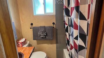 Une petite salle de bain comprenant des toilettes, un porte-serviettes, une fenêtre et un rideau de douche.