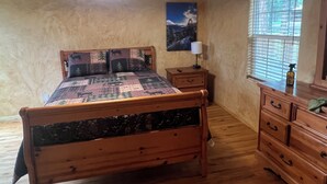 Ein hölzernes Bett mit einer Steppe, ein Nachttisch mit einer Lampe, eine Kommode und ein Fenster mit Jalousien.
