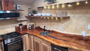Eine Küche mit Holzarbeitsplatte, einem Herd, einem Backofen und einem Geschirrspüler. Es gibt Regale mit Geschirr und eine Pflanze.