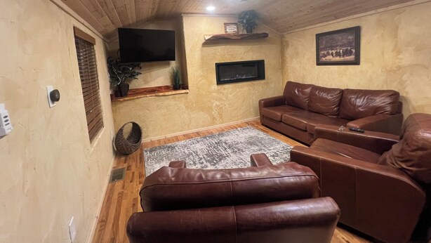 Ein Wohnzimmer mit einem braunen Ledersofa, einem an der Wand montierten Fernseher und einem Deckenventilator.