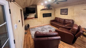Ein gemütliches Wohnzimmer mit einer braunen Ledersofa, einem Flachbildfernseher an der Wand und einem Deckenventilator.