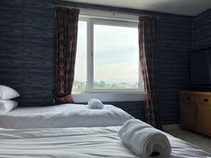 Ein Hotelzimmer mit einem Bett, einem Fenster mit Vorhängen, einem Fernseher und einem Holzschrank.