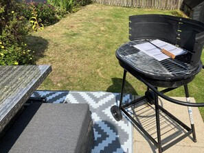 A barbecue grill with a metal grate and a wooden handle, placed on a patterned outdoor mat. - Beautiful 3-bedroom house. Sea view.  40 mins from Edinburgh. Dog friendly. (Burntisland)