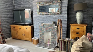 A hotel room with a television, a mirror, a patterned wall, a wooden cabinet, a small table, a chair, a sofa, and a lamp. - Beautiful 3-bedroom house. Sea view.  40 mins from Edinburgh. Dog friendly. (Burntisland)