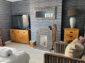 Una camera d'albergo con televisione, uno specchio, una parete decorata, un armadio in legno, un tavolino, una sedia, un divano e una lampada.