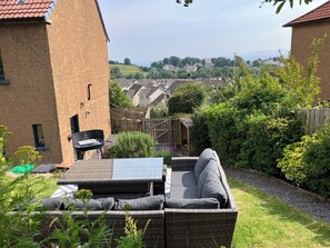 Un giardino sul retro con un divano in vimini, un barbecue e un capanno di legno.
