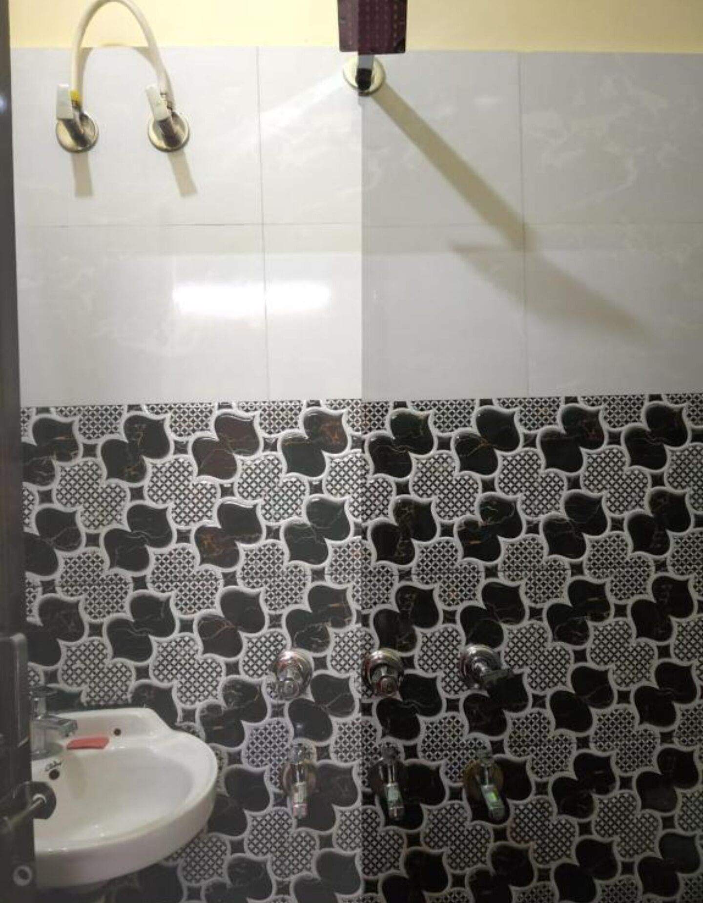 A bathroom with a white sink, a shower with a white tub, and a tiled wall with a black and white pattern.