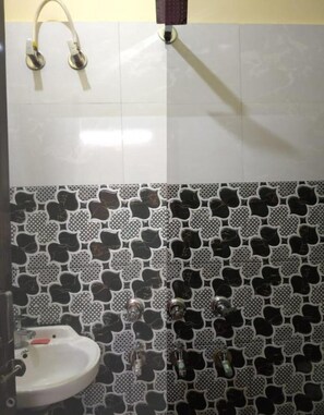 A bathroom with a white sink, a shower with a white tub, and a tiled wall with a black and white pattern. - Hotel Awadh Kailash (Bahraich)