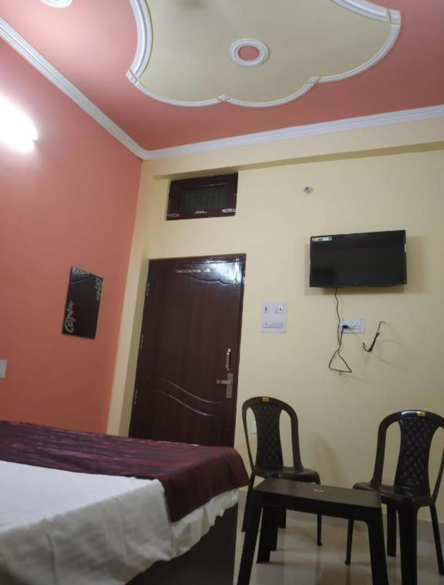 A bedroom with a bed, a TV mounted on the wall, and two chairs.