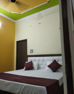 A hotel room with a bed, a door, and a light switch on the wall. - Hotel Awadh Kailash (Bahraich)