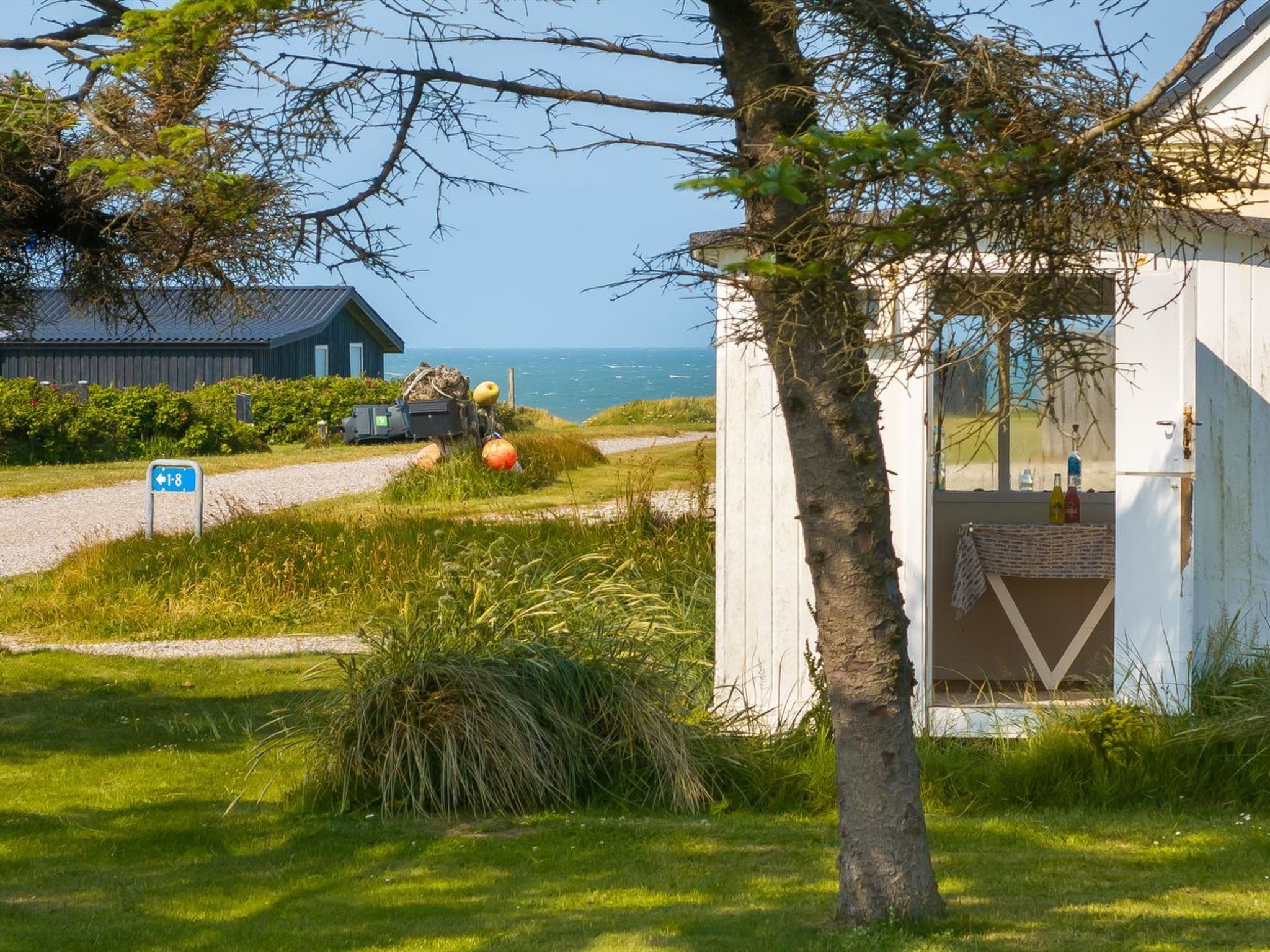 A coastal property with a small building, a clear view of the sea, and a sign indicating a path.