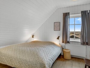 A bedroom with a sloped ceiling, a bed with a patterned bedspread, a window with curtains, and a framed picture on the wall. - "Filine" - 100m from the sea by Interhome (Løkken)