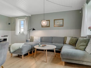 Un salon moderne avec un canapé d’angle gris, une table basse ronde et une suspension.