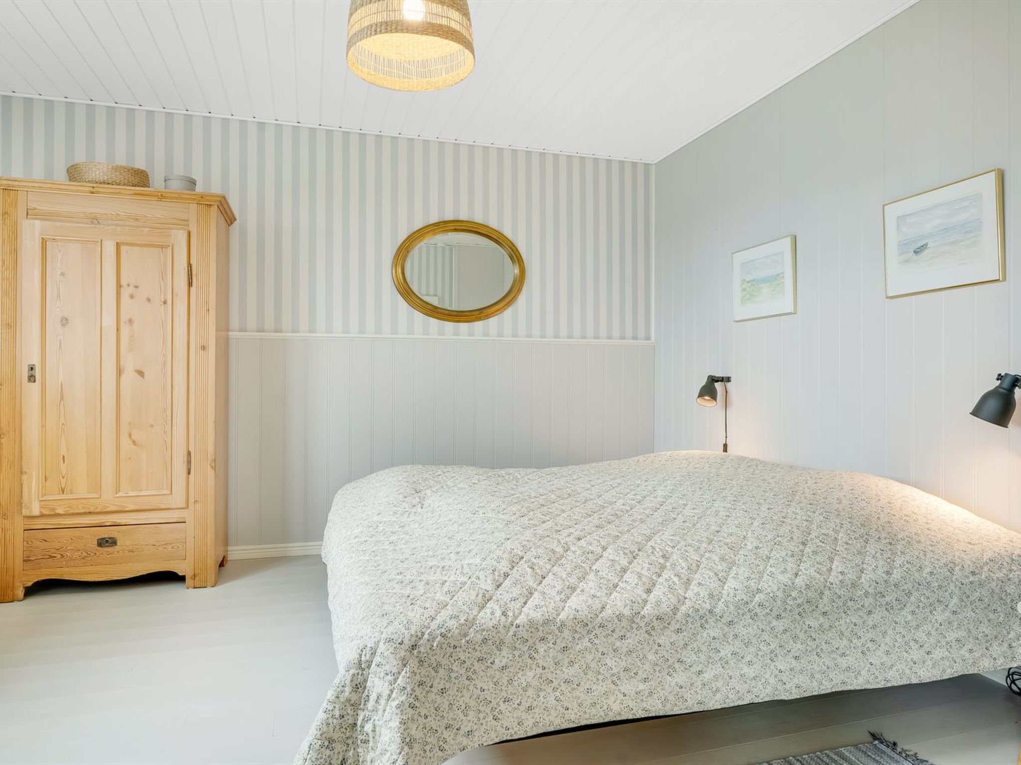 A bedroom with a bed, a wooden wardrobe, a round mirror, and two wall-mounted lamps.