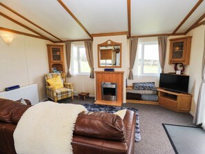 A cozy living room with a fireplace, a television, and a comfortable seating area. - The Lodge at Piece Farm (High Peak)
