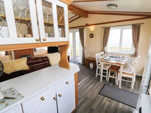 A compact kitchen with a dining area, wooden beams, a white countertop, and a view through the window. - The Lodge at Piece Farm (High Peak)