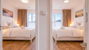 A mirrored view of a hotel room with two beds, a window with curtains, and a painting on the wall. - Vrbo Property (Olpenitz)
