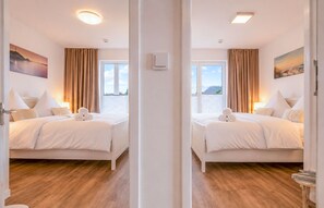 A mirrored view of a hotel room with two beds, a window with curtains, and a painting on the wall. - Vrbo Property (Olpenitz)