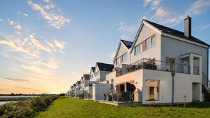 A row of modern houses with balconies, a grassy foreground, and a clear sky. - Vrbo Property (Olpenitz)