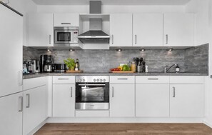 A modern kitchen with white cabinets, a Bosch oven, a microwave, and a coffee maker. - At the Marina – Vacation Rental with Ocean View, Sauna, and Hot Tub (Olpenitz)