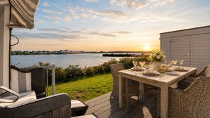 An outdoor dining area with a view of the water and sunset. - Vrbo Property (Olpenitz)