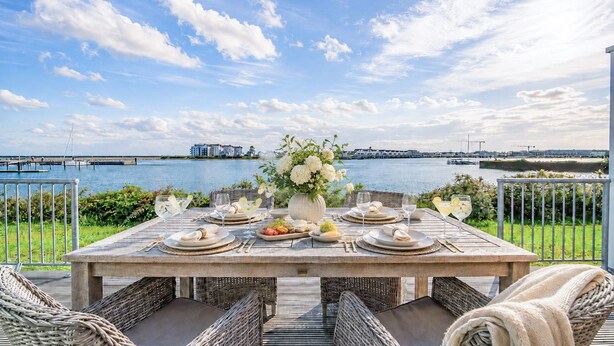 An outdoor dining area with a view of the water and buildings in the distance. - Vrbo Property (Olpenitz)