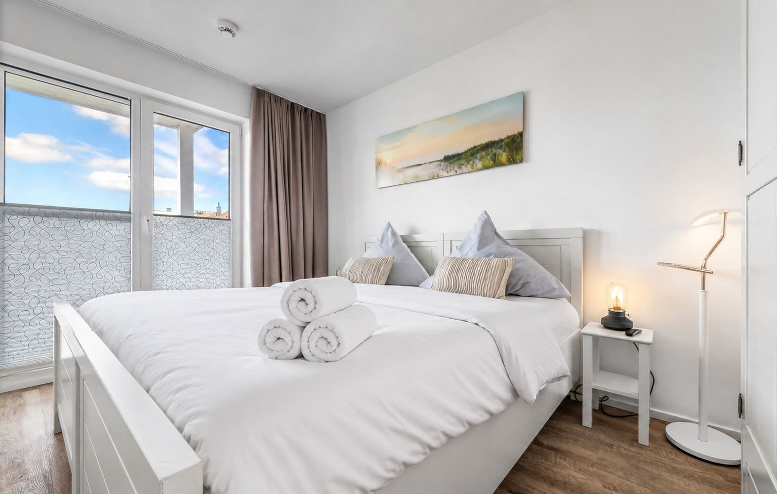 Une chambre moderne avec un grand lit, une table de chevet avec une lampe et une fenêtre avec des rideaux.