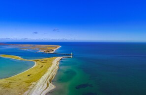 An aerial view of a coastal area with a lighthouse, sandy beaches, and clear blue waters. - Vrbo Property (Olpenitz)
