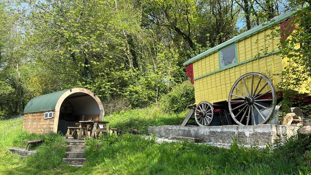 Eine rustikale Holzhütte mit einem grünen Dach, einer kleinen Veranda und einem großen hölzernen Wagenrad.