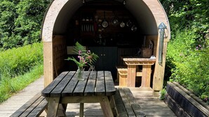 Ein hölzerner Essbereich im Freien mit einem Tisch und Bänken, umgeben von viel Grün.