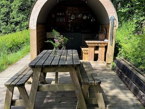 A wooden outdoor dining area with a table and benches, surrounded by greenery. - PRUDENCE, pet friendly, character holiday cottage in Ashwater (East Panson)
