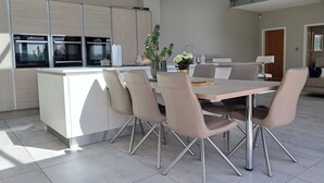 Ett modernt kök med en central köksö, rostfria vitvaror och en matplats med stolar och ett bord.