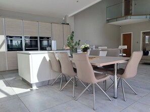 Een moderne keuken met een centraal eiland, roestvrijstalen apparatuur en een eetgedeelte met stoelen en een tafel.